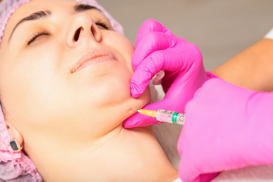 The Cosmetologist Makes Lipolytic Injection on the Chin of a Young Woman against the Double Chin in a Beauty Salon.